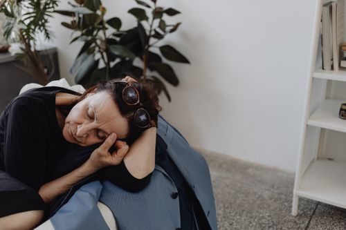 Free A senior woman resting on a couch with closed eyes, displaying mild sadness. Indoor setting. Stock Photo