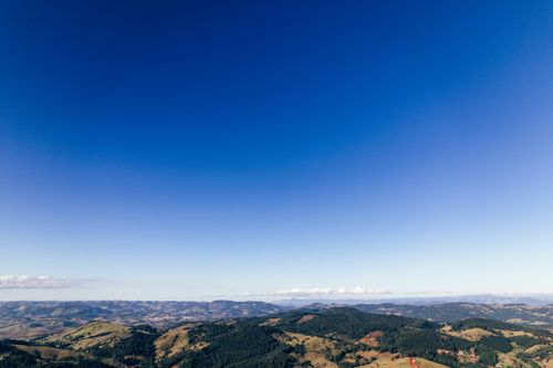 Free Aerial view of scenic landscape of wild nature and azure blue sky with some distant clouds above lush mountains and valleys with settlement Stock Photo