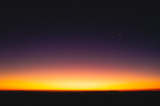 Spectacular landscape of bright colorful sundown on horizon and dark purple sky above with glowing moon in twilight evening time