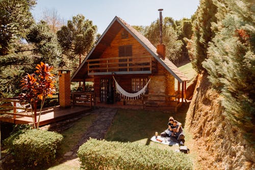 A Couple Sitting on a Picnic Blanket Near the Beautiful Wooden House