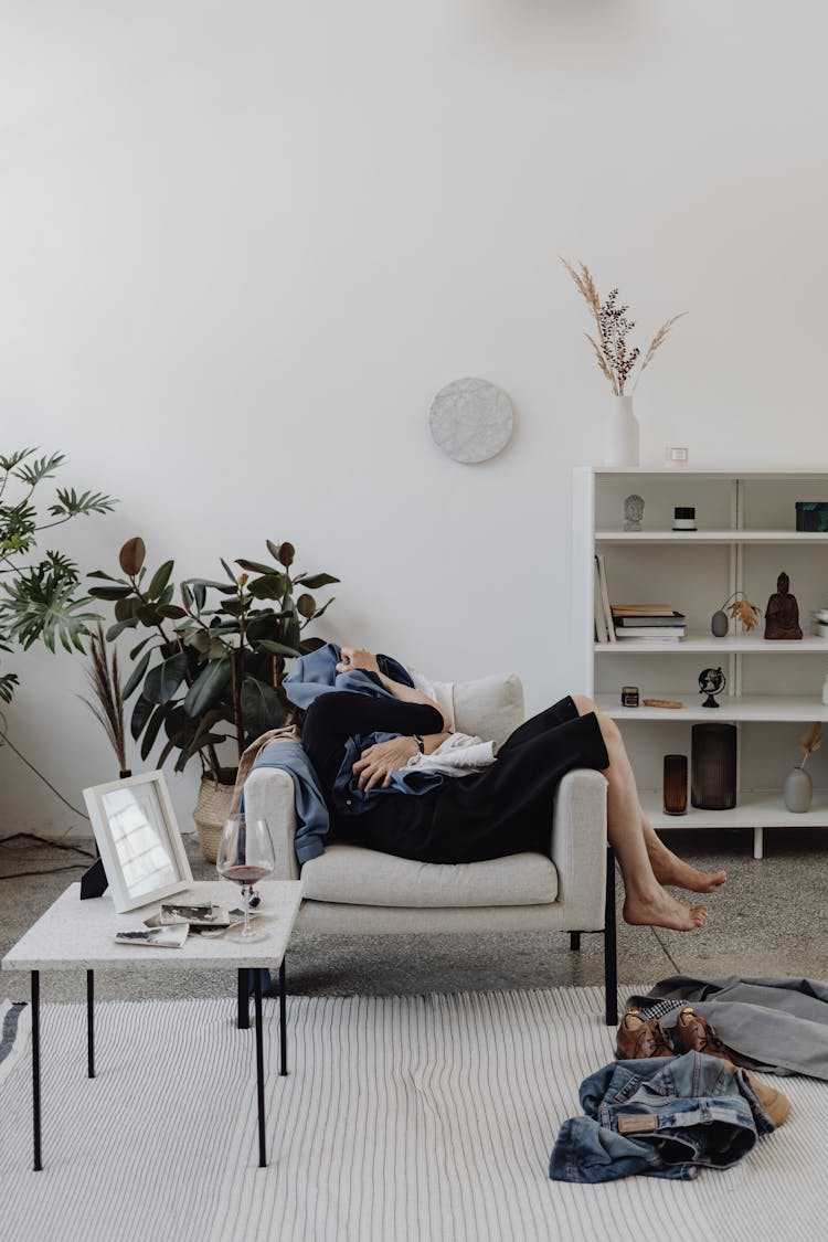 A Person Resting On A Couch While Covering Herself Using The Clothes She Is Holding