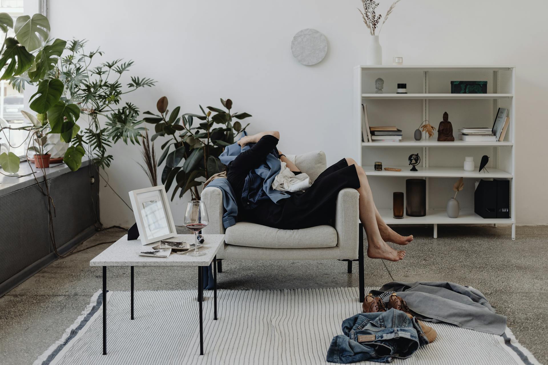 A person resting on a sofa in a cozy living room with plants and a glass of wine.