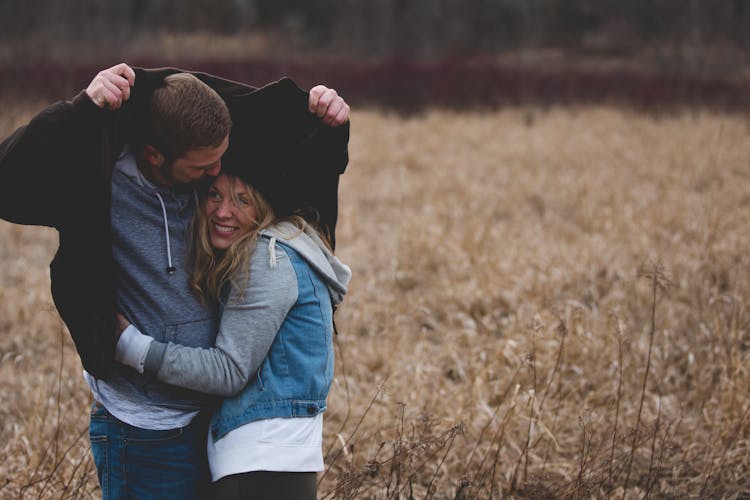 Man And Woman Hugging On Brown Field