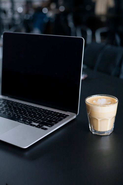 Free A sleek laptop and a latte on a dark tabletop, conveying modern work ambiance. Stock Photo
