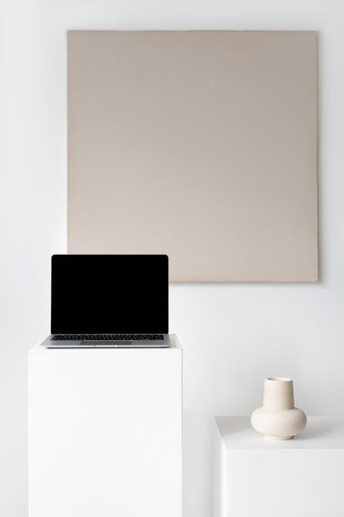 A Laptop on a White Platform Beside a Ceramic Vase