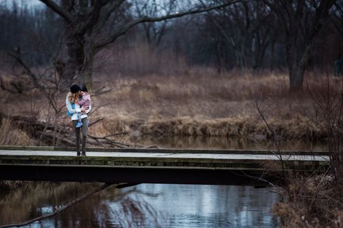 Free A mother holding her child on a bridge in a serene forest landscape. Stock Photo