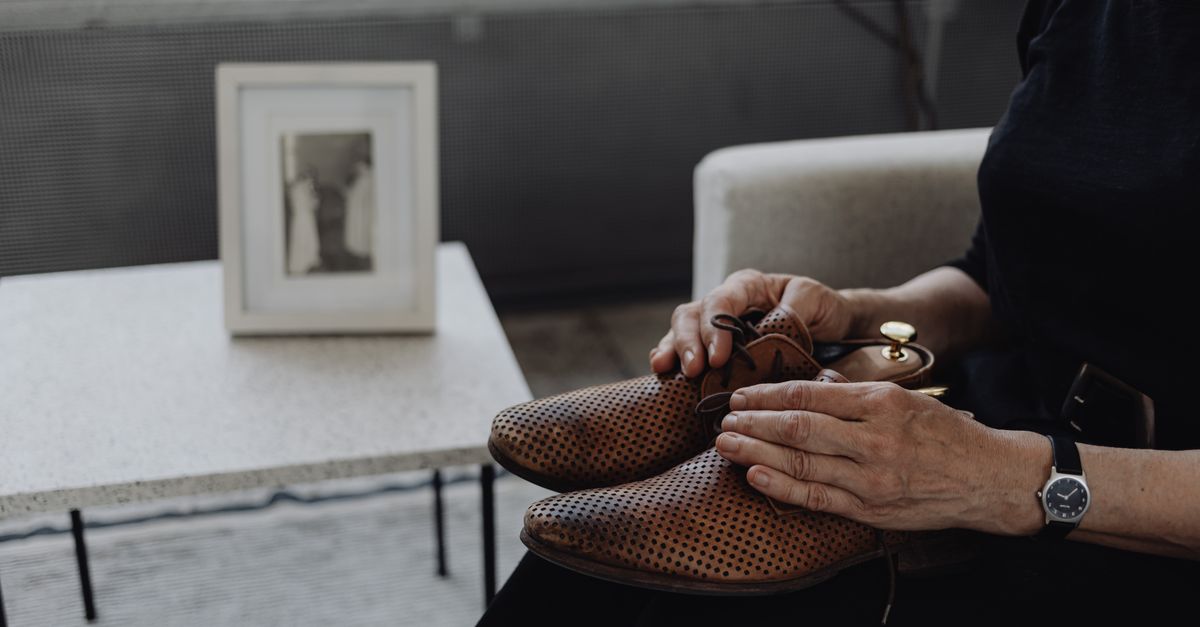 A person sits holding brown leather shoes, reflecting on memories.