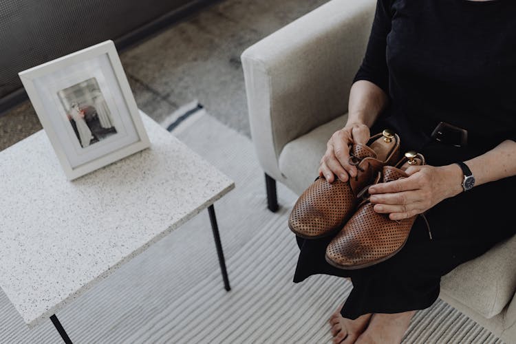 A Person In Black Clothes Holding Brown Leather Shoes