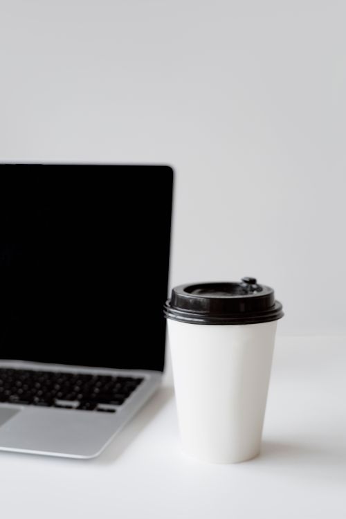 Free A clean, minimalist desk setup with a disposable coffee cup next to a laptop, suitable for modern workspaces. Stock Photo