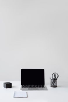A clean and minimalist workspace featuring a laptop, notepad, and pen holder on a white desk.