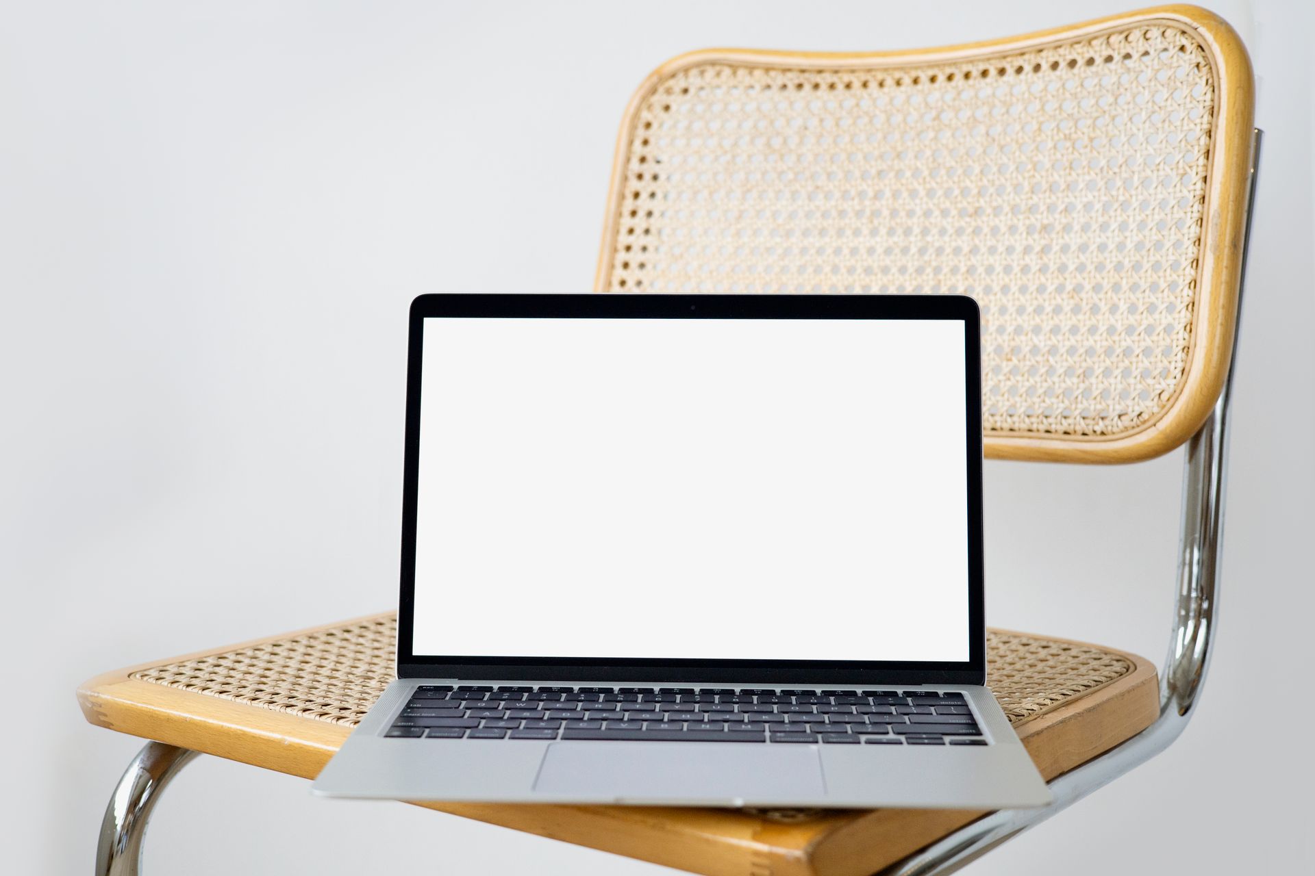 Modern laptop with a blank screen on a woven chair, perfect for digital presentations.