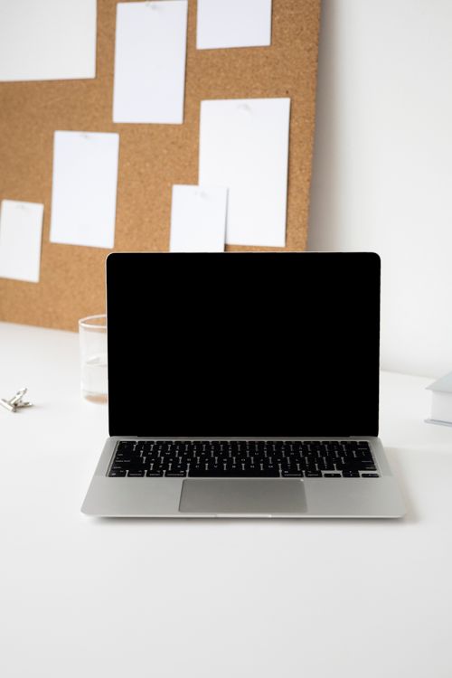 Free Elegant workspace showing a blank laptop screen with a corkboard and white sheets as background for design concepts. Stock Photo