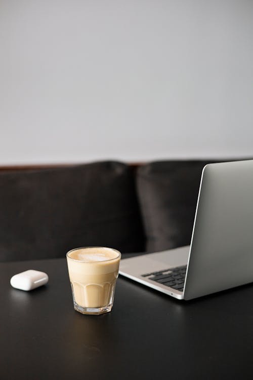 A Glass of Coffee Beside a Laptop on a Desk