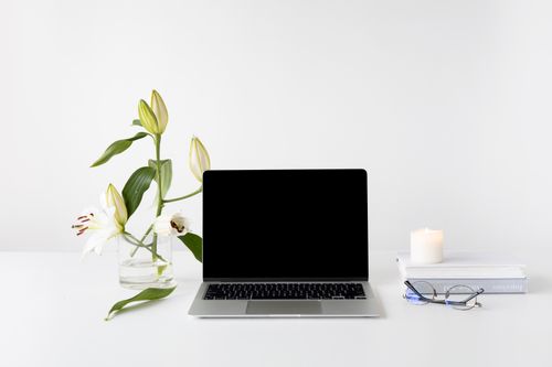 Free Elegant minimalist desk setup with laptop, white lilies, books, and candle. Stock Photo