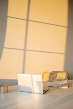 A sunlit office space featuring a laptop and notebook on a white desk, creating a warm atmosphere.