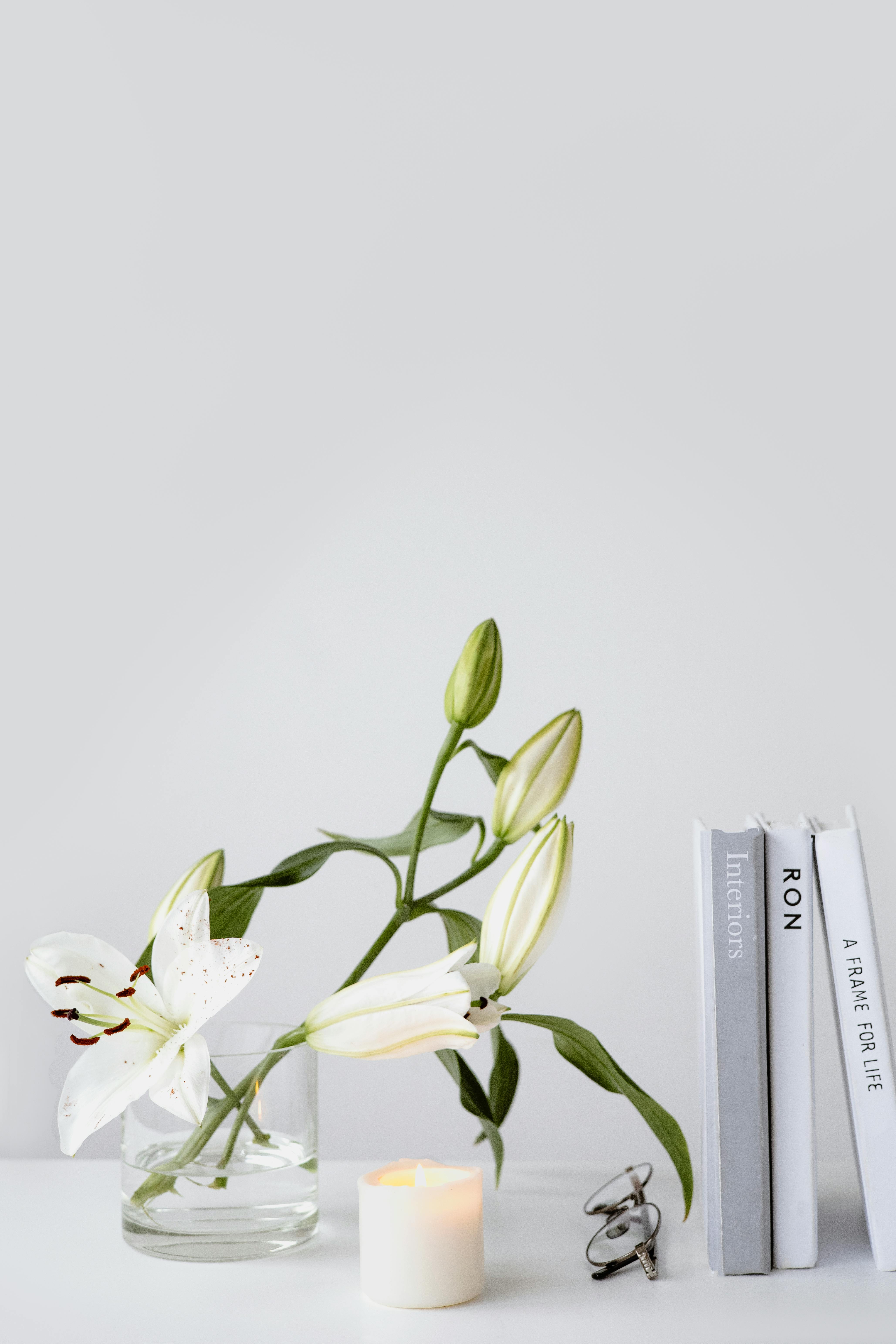 A serene minimalist interior scene with white lilies, a candle, and books on a table.