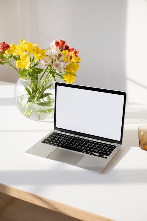 Laptop with Blank Screen Beside a Bunch of Flowers in a Clear Fishbowl