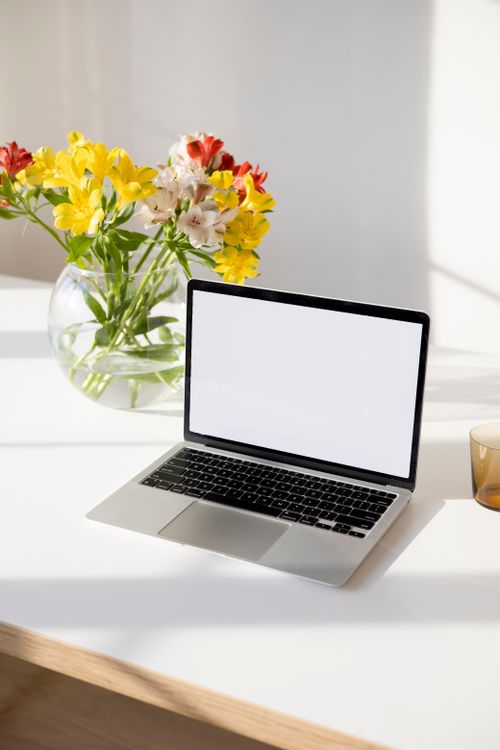 Free A laptop with a blank screen on a desk, adorned with colorful flowers in a vase, creating a lively workspace. Stock Photo