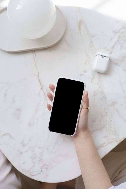 Free A person holding a smartphone on a marble table with AirPods nearby, ideal for tech and lifestyle themes. Stock Photo
