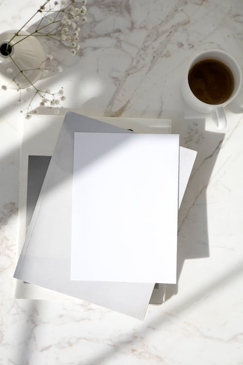 Stack of Blank White Paper Sheets and a Cup of Coffee on a Table