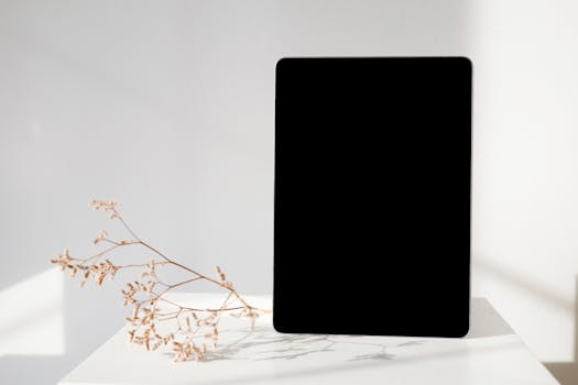 A tablet on a white surface beside dried flowers, showcasing a minimalist design.