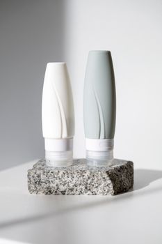 Minimalist product shoot of two cosmetic bottles on a stone platform.
