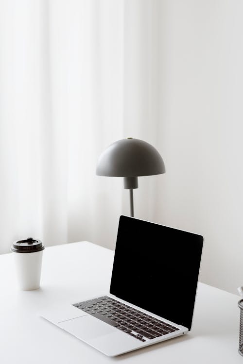 A Laptop and Paper Cup on White Table