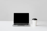 Photo of a Laptop Beside a White Paper Cup