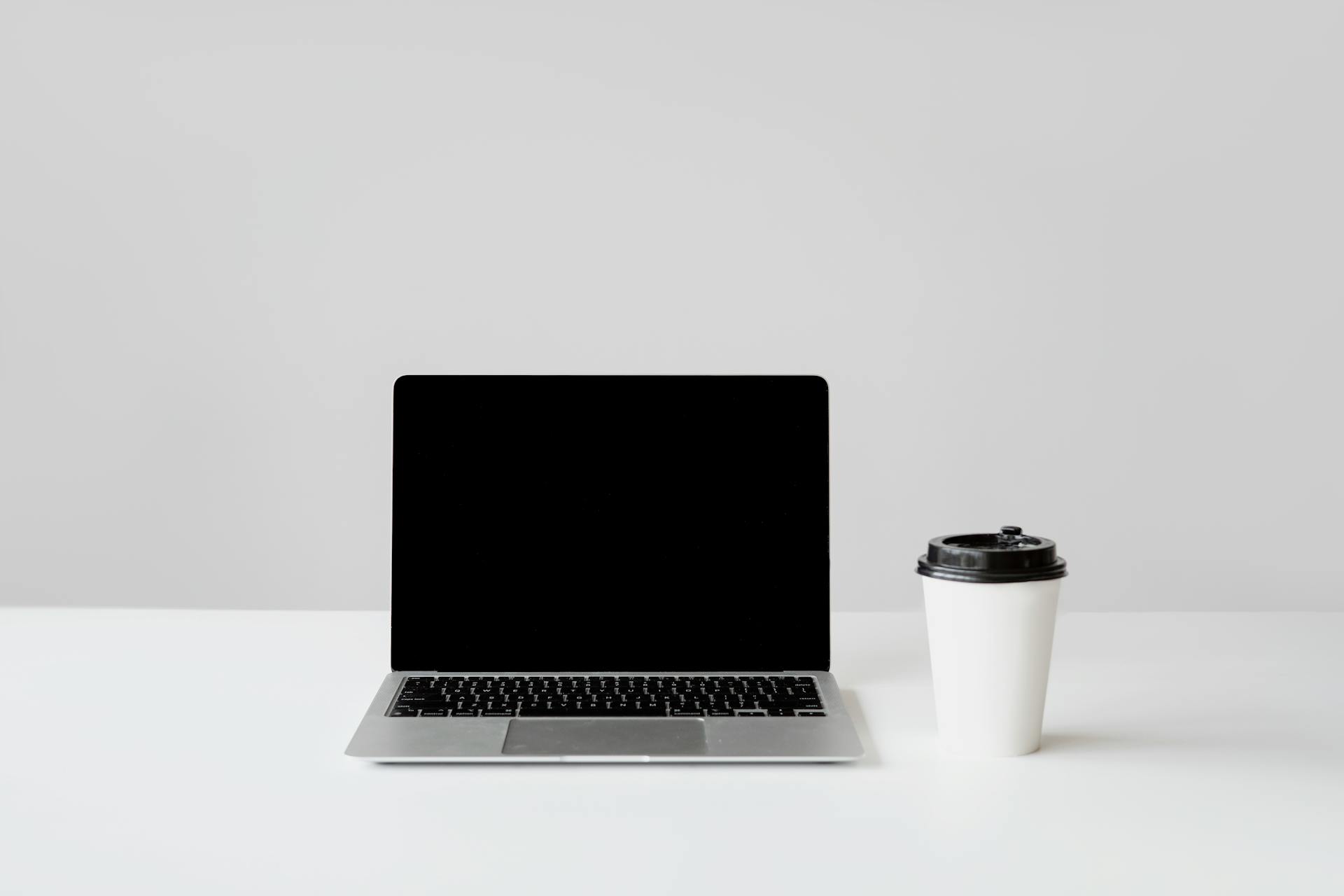 Simple workspace setup with a laptop and coffee cup on a white desk.