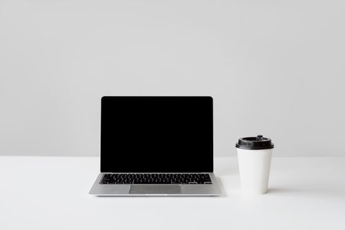 Free Simple workspace setup with a laptop and coffee cup on a white desk. Stock Photo