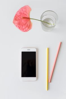 A minimalist flat lay featuring a smartphone, colored pencils, and a flower vase on a white background.
