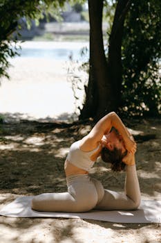 Woman practicing yoga one-legged pigeon pose outdoors in sunny forest.