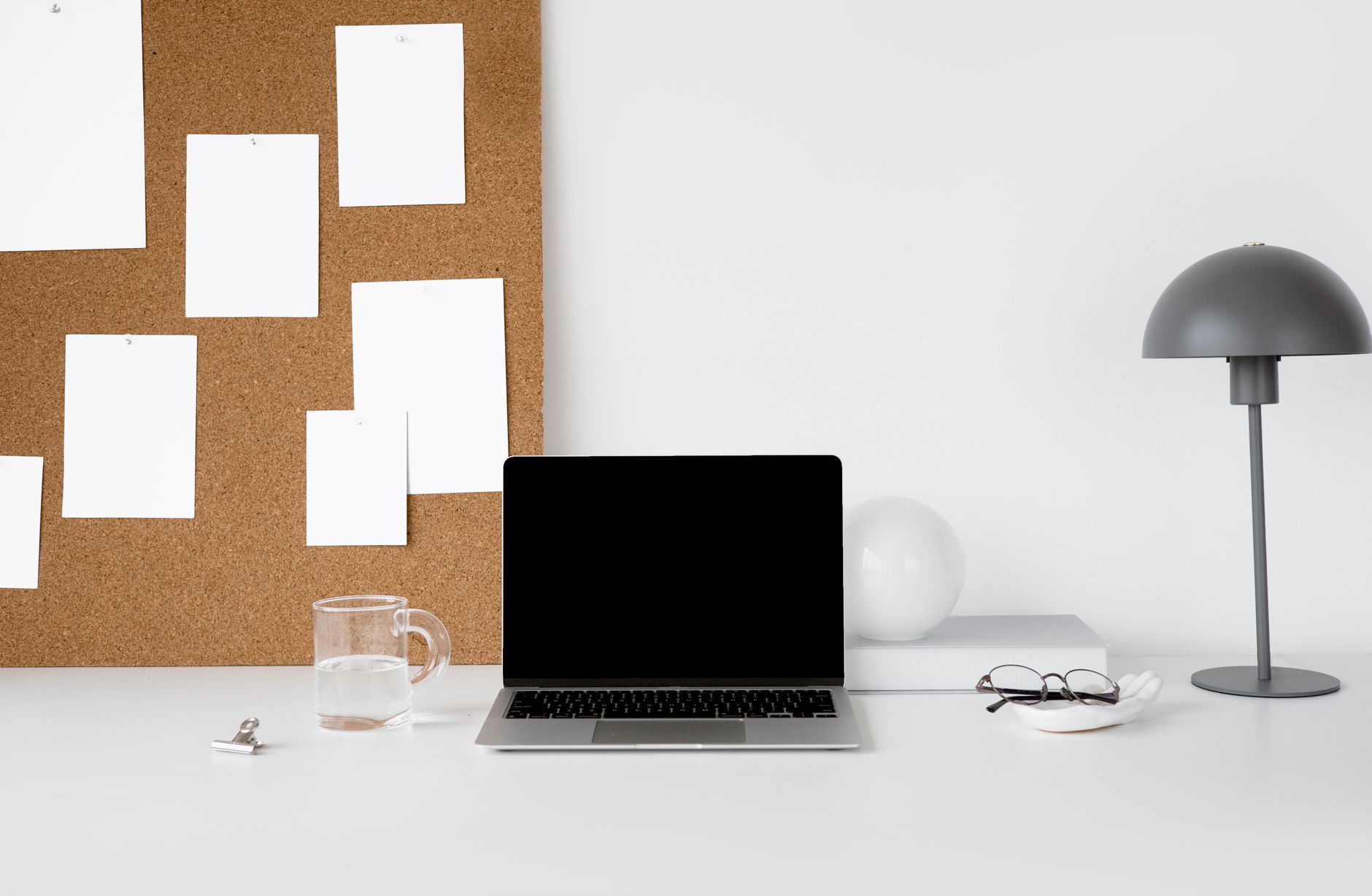 Espacio de trabajo minimalista con un portátil, tablón de corcho y lámpara para un aspecto elegante y profesional.