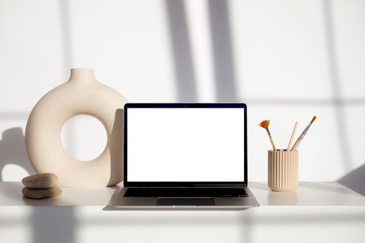 Elegant minimalist workspace with laptop, ceramics, and brushes in natural light.