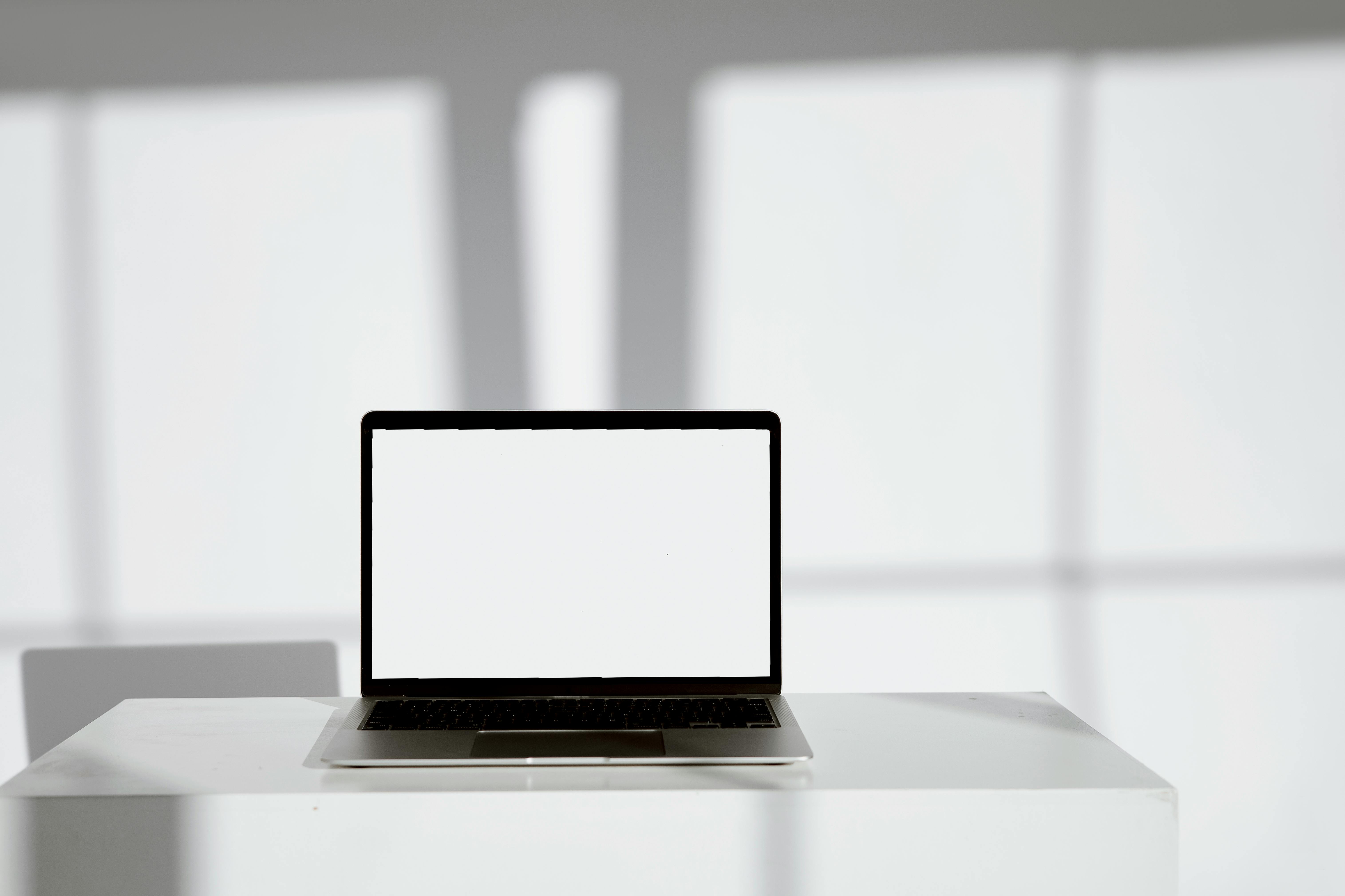 Blank laptop screen on a modern white desk in a bright, sunlit room.