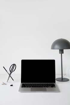 Sleek and modern workspace setup with laptop, lamp, and stationery on a white desk.