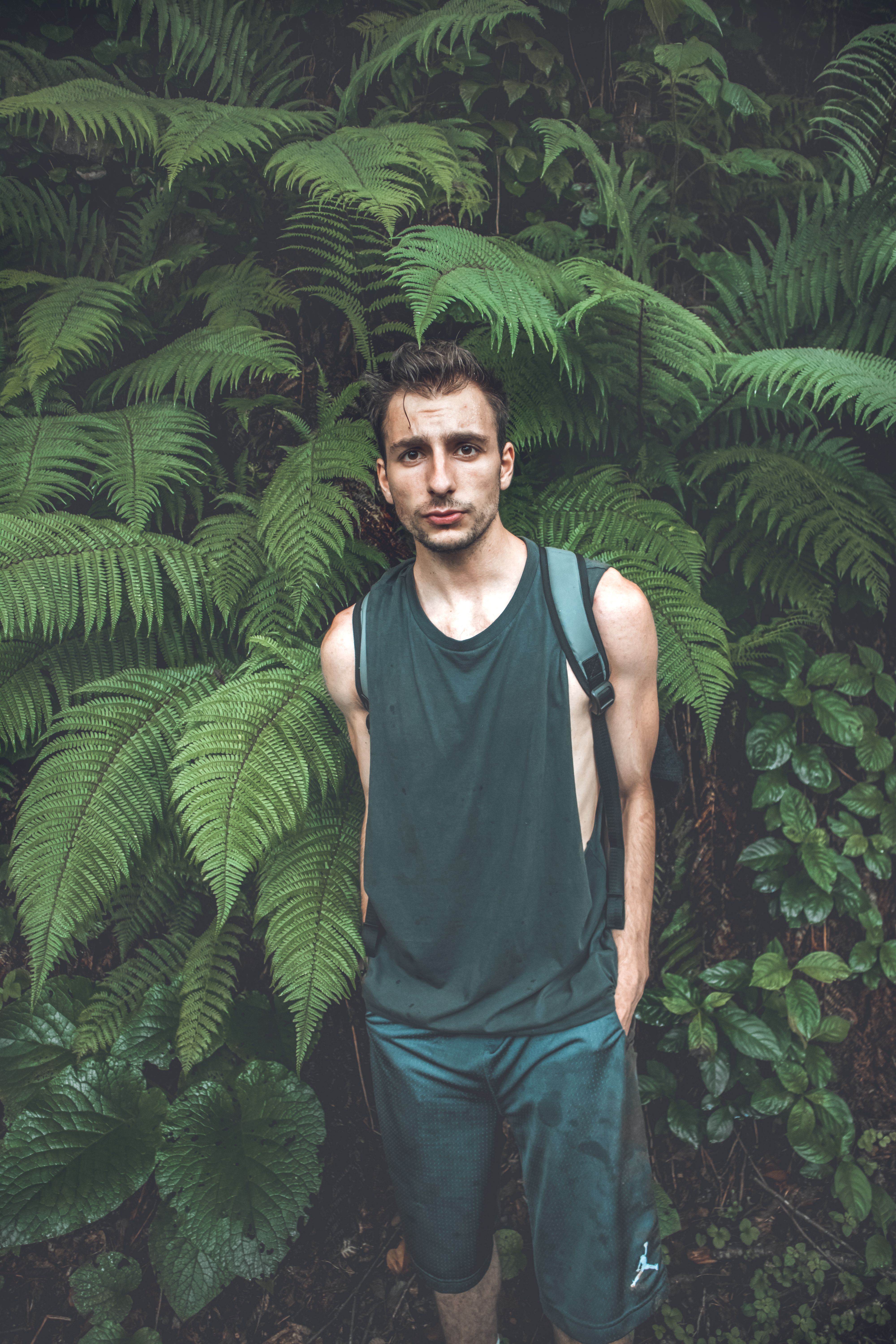 Portrait of a young man in a jungle setting, surrounded by lush green ferns.