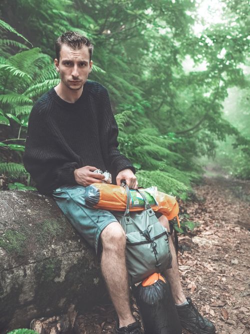 Free A young man takes a break with his backpack in a foggy, lush green forest. Stock Photo