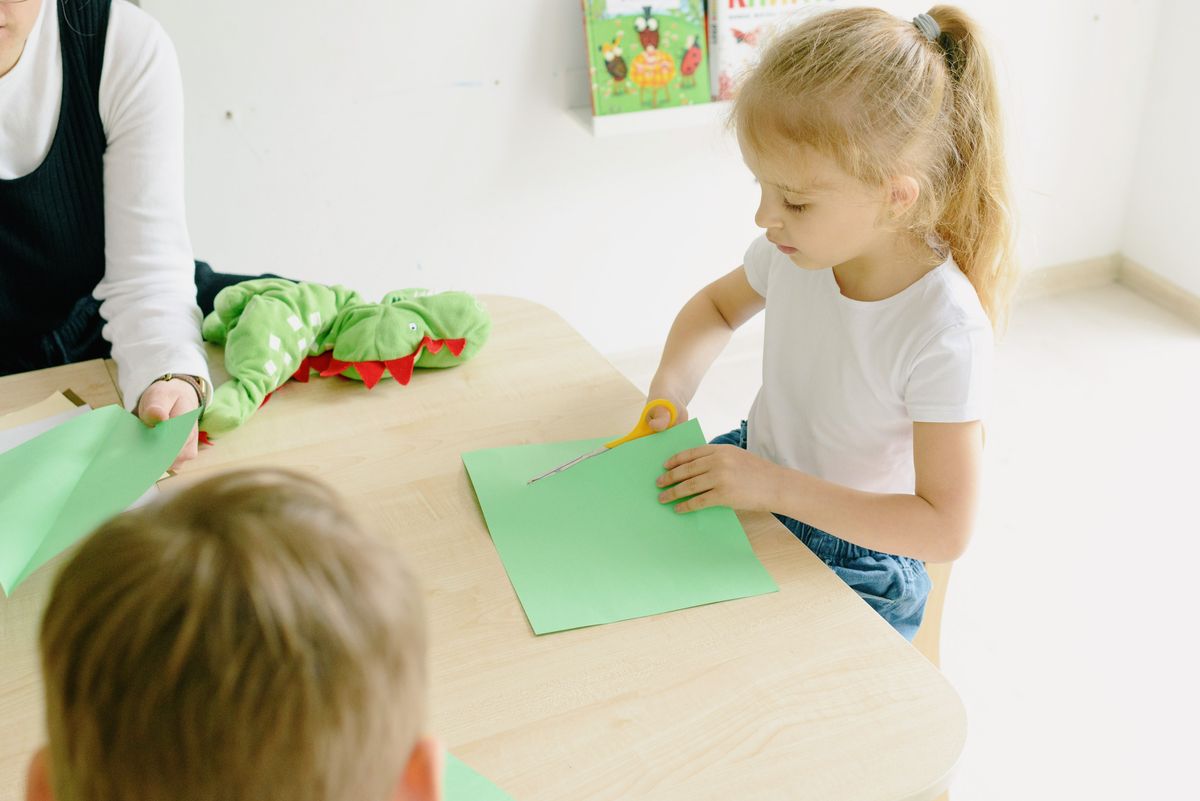 Young girl cutting green paper leaves at a classroom table