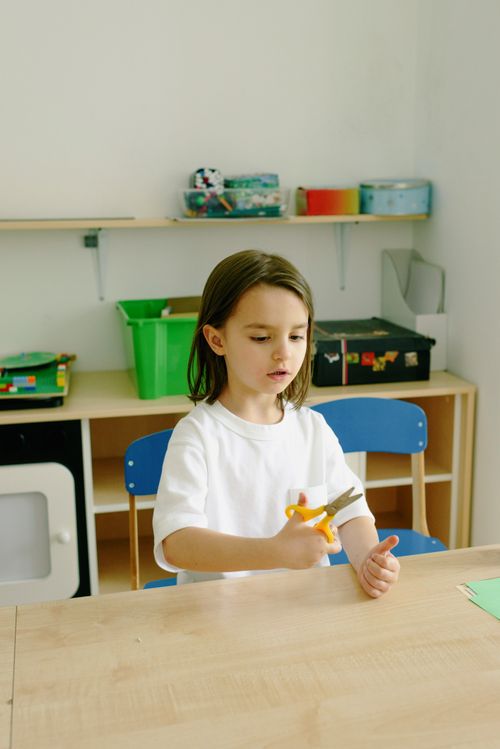 Free Young child in a classroom setting using scissors for a craft project, focused and creative. Stock Photo