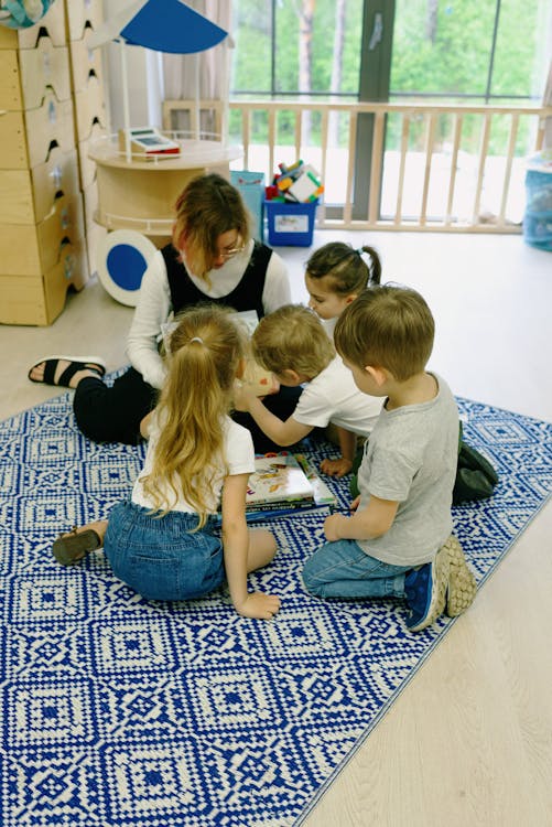 Free Young children and teacher in a kindergarten reading session indoors. Stock Photo
