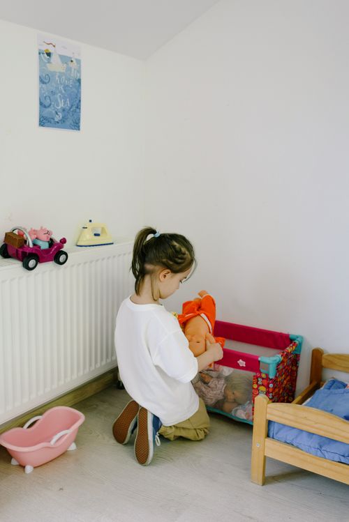 Free Young girl sits on the floor and plays with dolls in a bright, cozy bedroom. Stock Photo