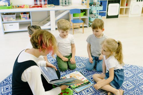Free Group of children and a teacher reading together indoors at preschool. Stock Photo
