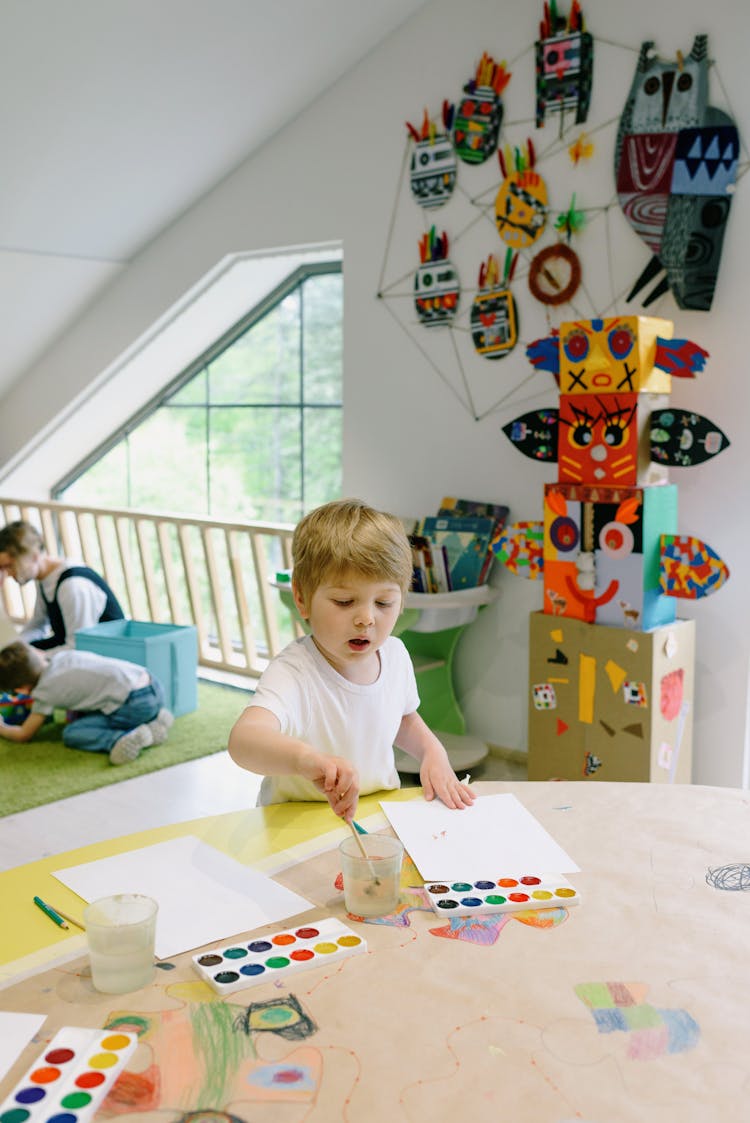 A Boy Sitting At The Table While Painting