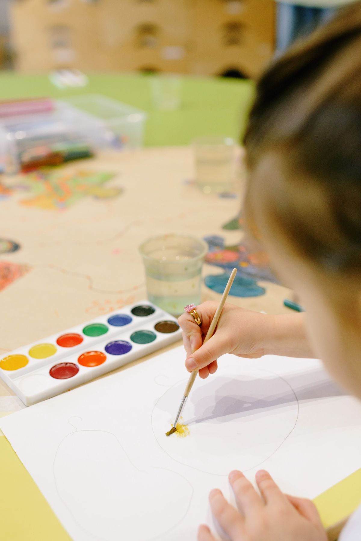 Child using watercolors to paint a picture on paper in a classroom
