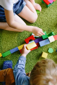 Children engaged in playful activities with vibrant blocks on a green carpet.