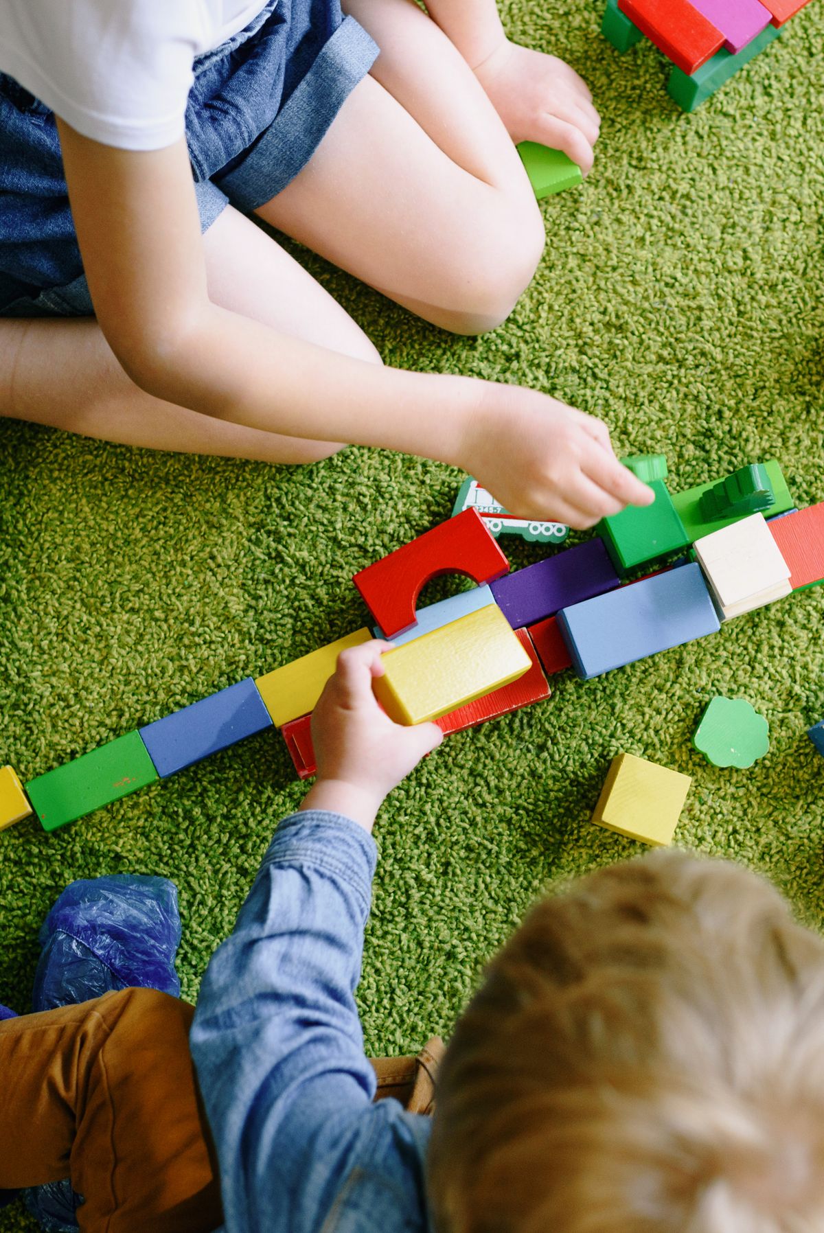 Children playing with vibrant blocks on a green carpet near felt-lined drawers that keep LEGO storage quiet