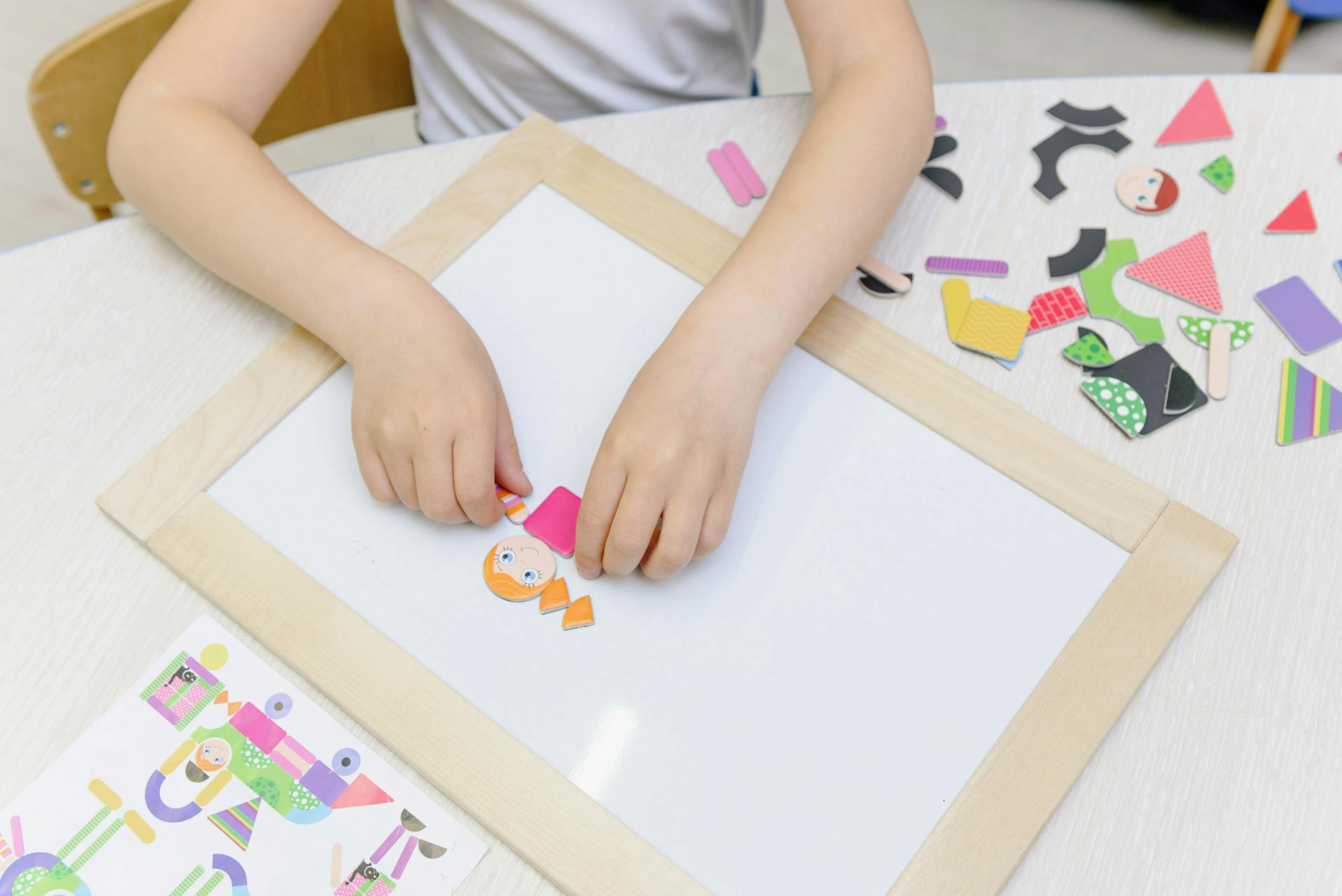A child assembling colorful cutout figures on a magnetic board, fostering creativity and learning.
