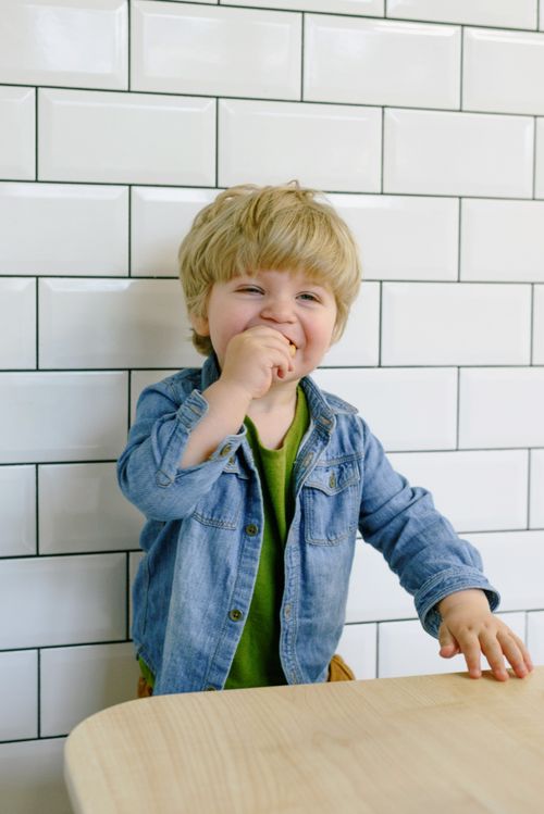 Free Adorable smiling child in a denim jacket inside a tiled room, captured candidly. Stock Photo