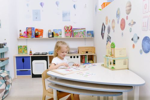 Free A young girl in a kindergarten classroom engaged in creative activities, surrounded by educational decor and toys. Stock Photo
